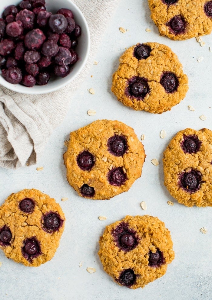 Oatmeal blueberry cookies on a counter next to a bowl of frozen blueberries.