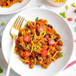 Plate of red lentil spiral pasta, topped with black beans, tomatoes, cheese, and green onions.