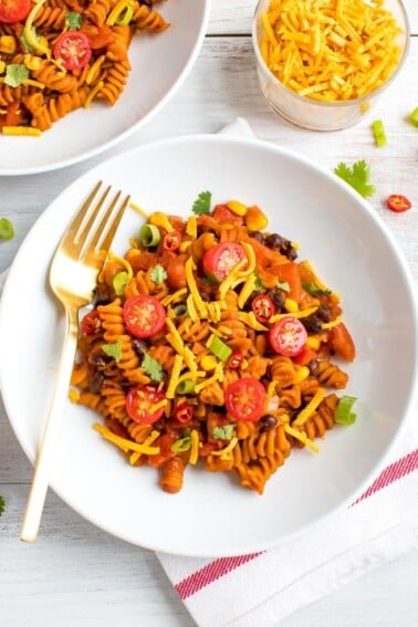 Plate of red lentil spiral pasta, topped with black beans, tomatoes, cheese, and green onions.