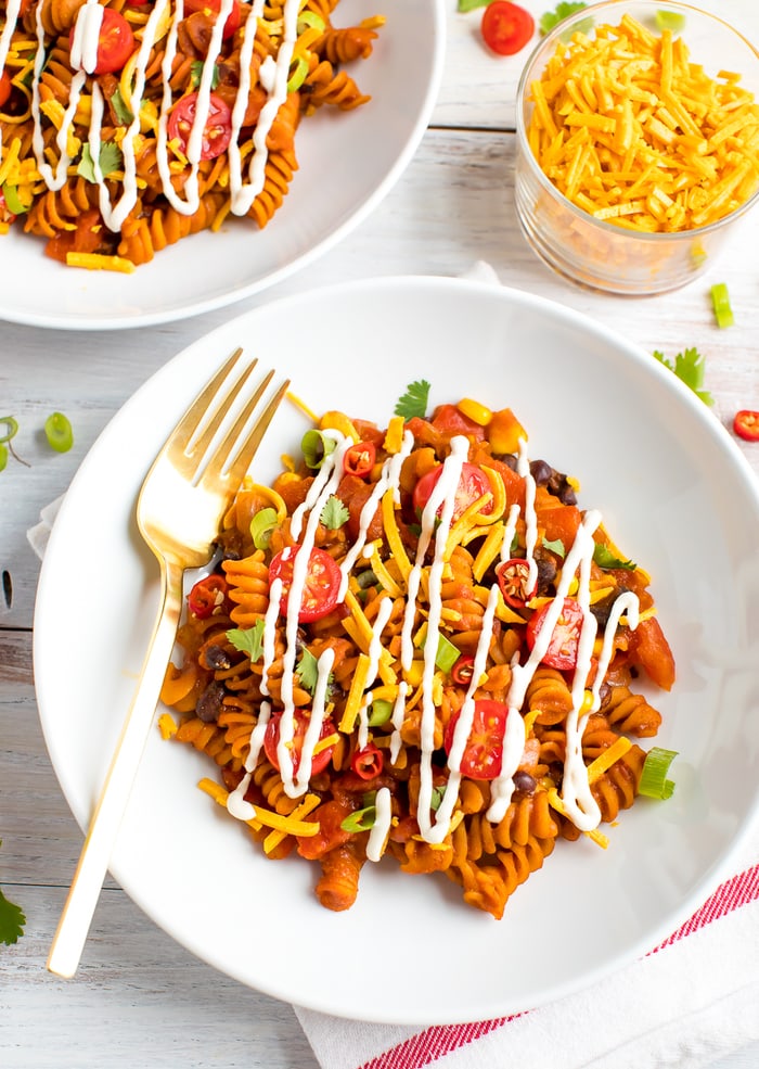 Plate of enchilada pasta mixed with tomatoes, green onions, peppers, corn, black beans, and topped with cheese and sour cream.