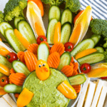 Cute turkey thanksgiving veggies tray. Veggies formed to look like a cute turkey as a veggie tray, with a bowl of guacamole. Text above reads "Thanksgiving Veggie Tray"