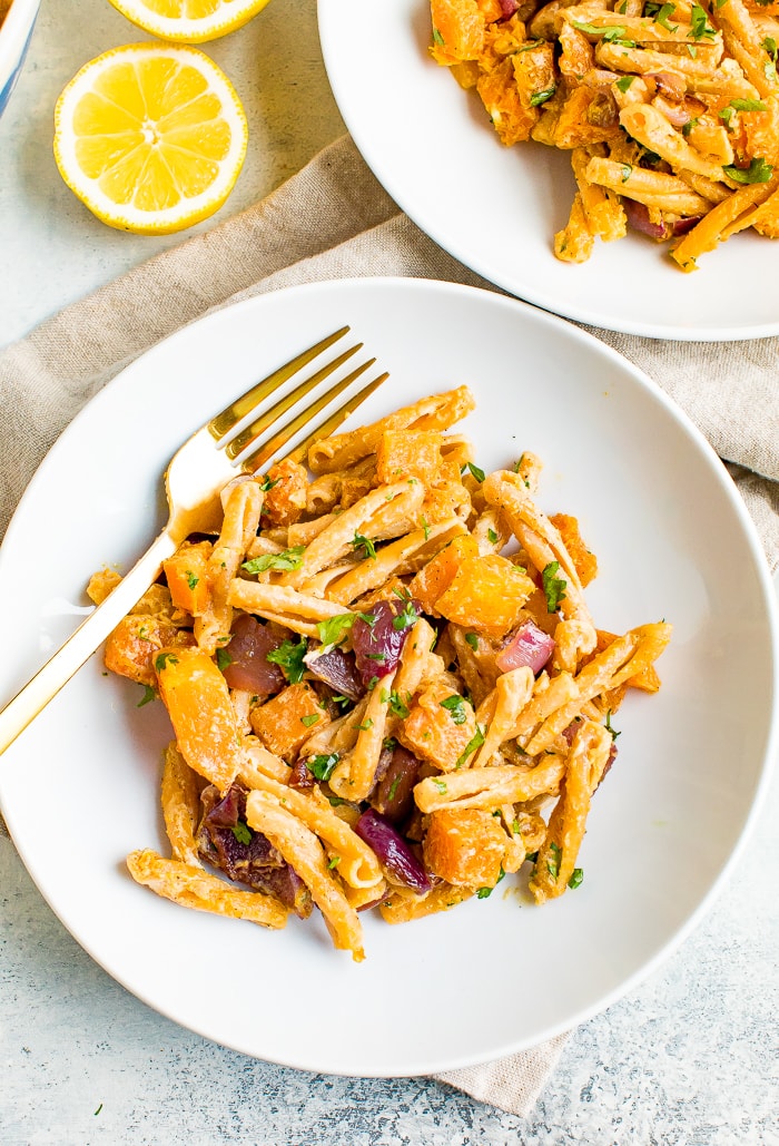 Plate of roasted butternut squash pasta with tahini sauce. Slices of lemon beside the plates.