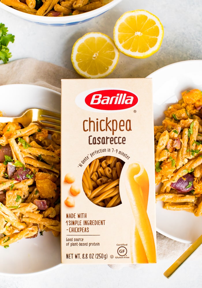 Box of chickpea casarecce Barilla pasta between two plates of roasted butternut squash pasta with tahini sauce. Lemon and sprigs of fresh cilantro are on the table.