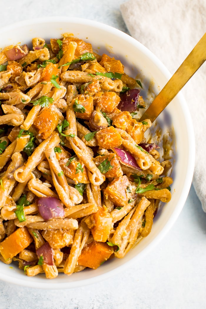 Serving bowl and spoon with roasted butternut squash pasta with tahini sauce. Chickpea pasta with roasted butternut squash, onions, and fresh cilantro.