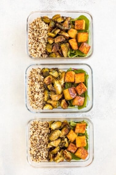 Three glass meal prep containers filled with sections of quinoa, roasted Brussel sprouts, greens and maple mustard tempeh cubes.