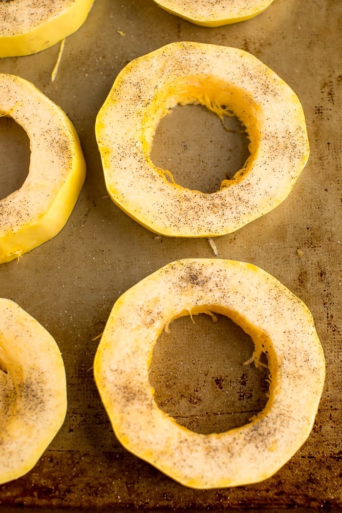 Rings of sliced spaghetti squash on a roasting pan, topped with olive oil, salt and pepper.