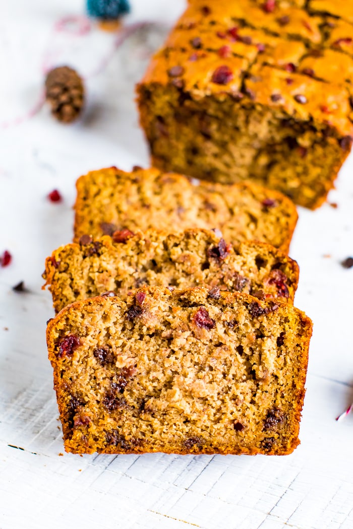 Slices loaf of gluten-free, dairy-free, cranberry chocolate chip banana bread with holiday decor on the table.