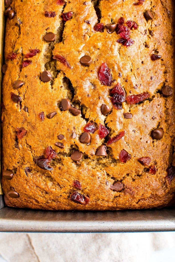 Cranberry chocolate chip banana bread in a pan, and topped with more chocolate chips and cranberries.