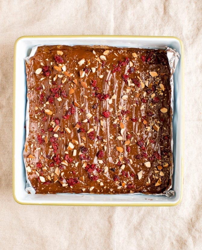Baking dish with gluten-free Christmas Crack, topped with melted chocolate, chopped almonds, and cranberries.