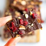 Hand holding a piece of healthy Christmas Crack, topped with almonds and cranberries.