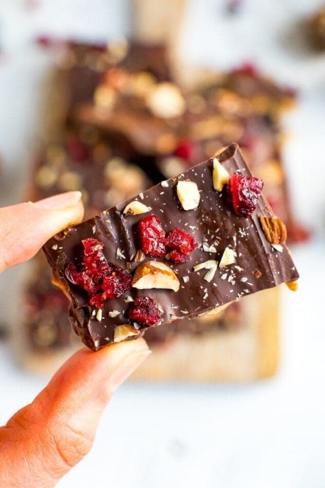 Hand holding a piece of healthy Christmas Crack, topped with almonds and cranberries.