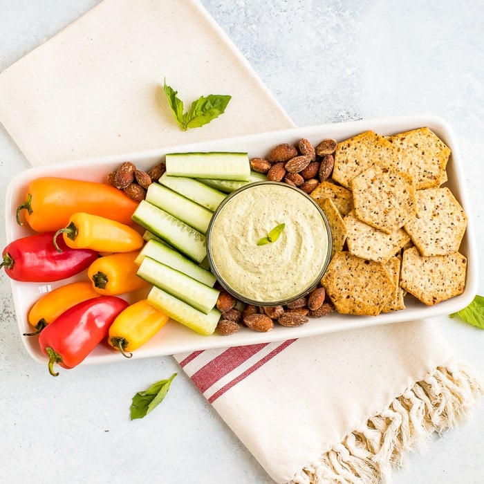 Almond Pesto Dip in a bowl and on a snack tray with cucumbers, almonds, mini peppers, and crackers.