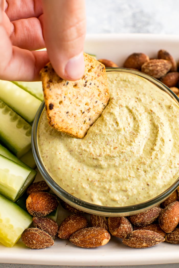 Cracker dipping into a creamy, low carb, Almond Pesto Dip.