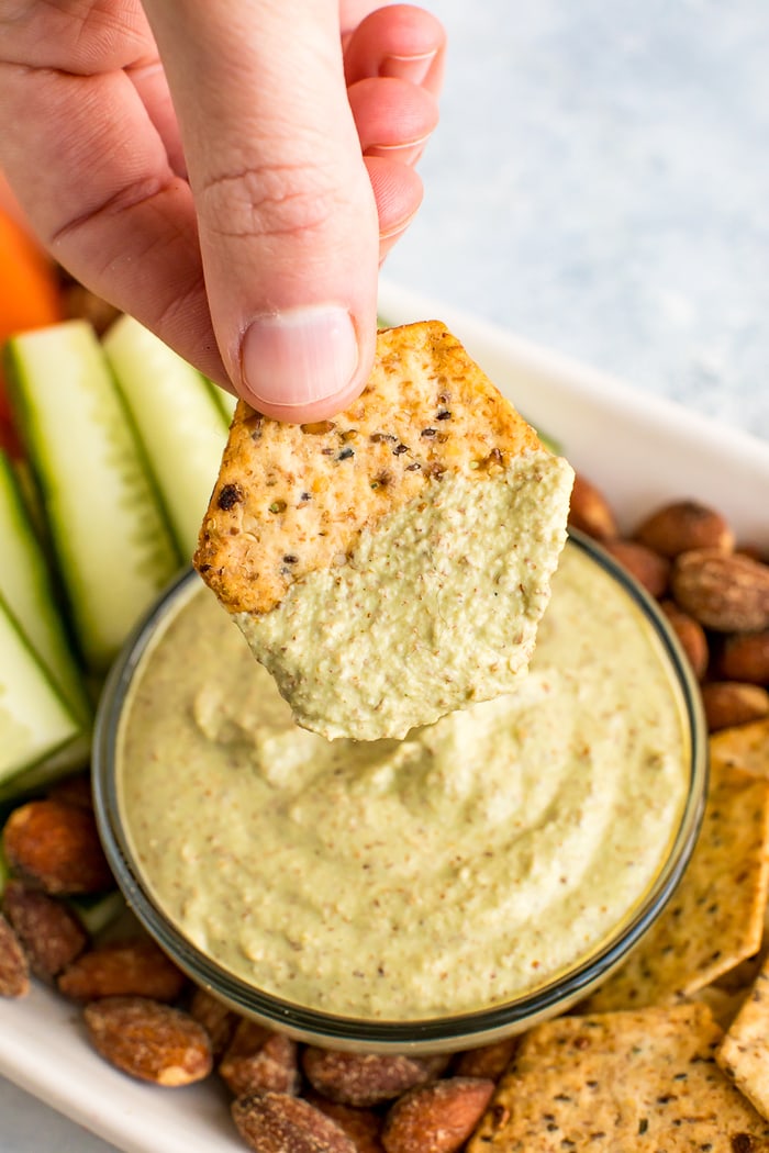 Cracker dipping into a creamy, low carb, Almond Pesto Dip.