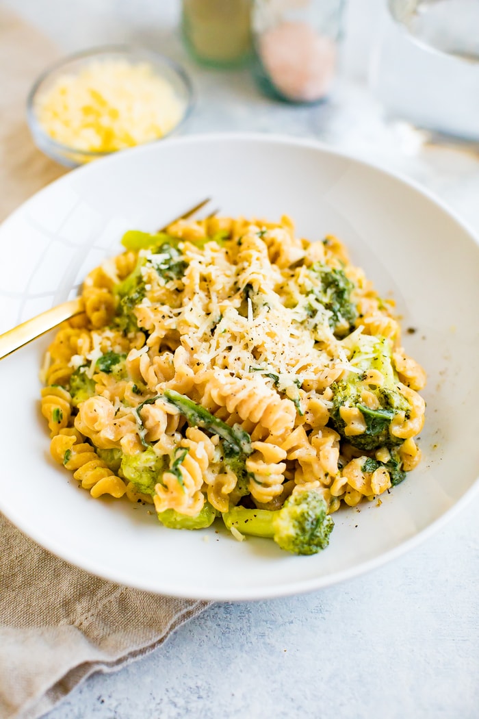 A bowl of creamy, healthy protein packed mac and cheese made with chickpea pasta, broccoli and spinach. Macaroni is topped with extra cheddar.