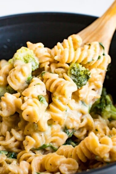 Wooden spoon mixing a pot of creamy and healthy protein mac and cheese made with chickpea pasta, broccoli and spinach.