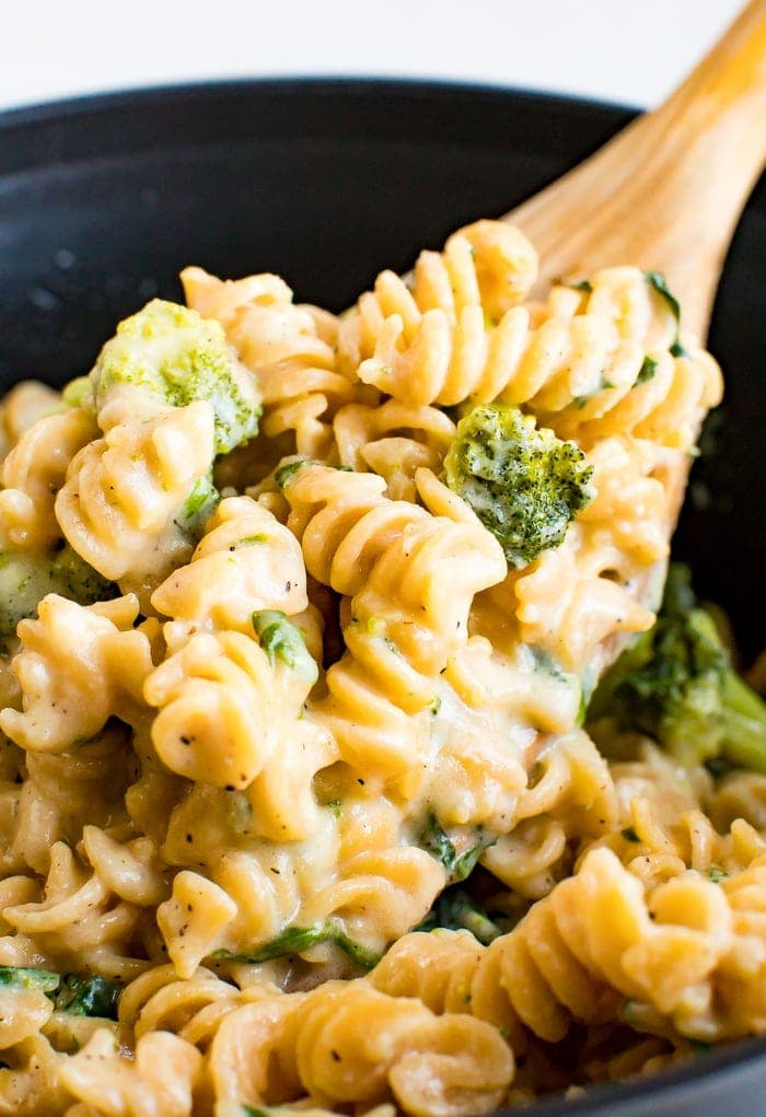 Wooden spoon mixing a pot of creamy and healthy protein mac and cheese made with chickpea pasta, broccoli and spinach.