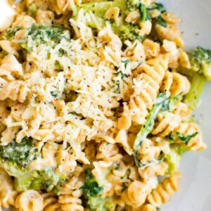 A bowl of creamy, healthy protein packed mac and cheese made with chickpea pasta, broccoli and spinach. Macaroni is topped with extra cheddar.