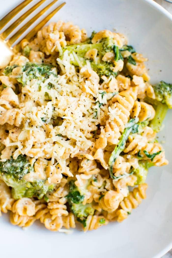 A bowl of creamy, healthy protein packed mac and cheese made with chickpea pasta, broccoli and spinach. Macaroni is topped with extra cheddar.