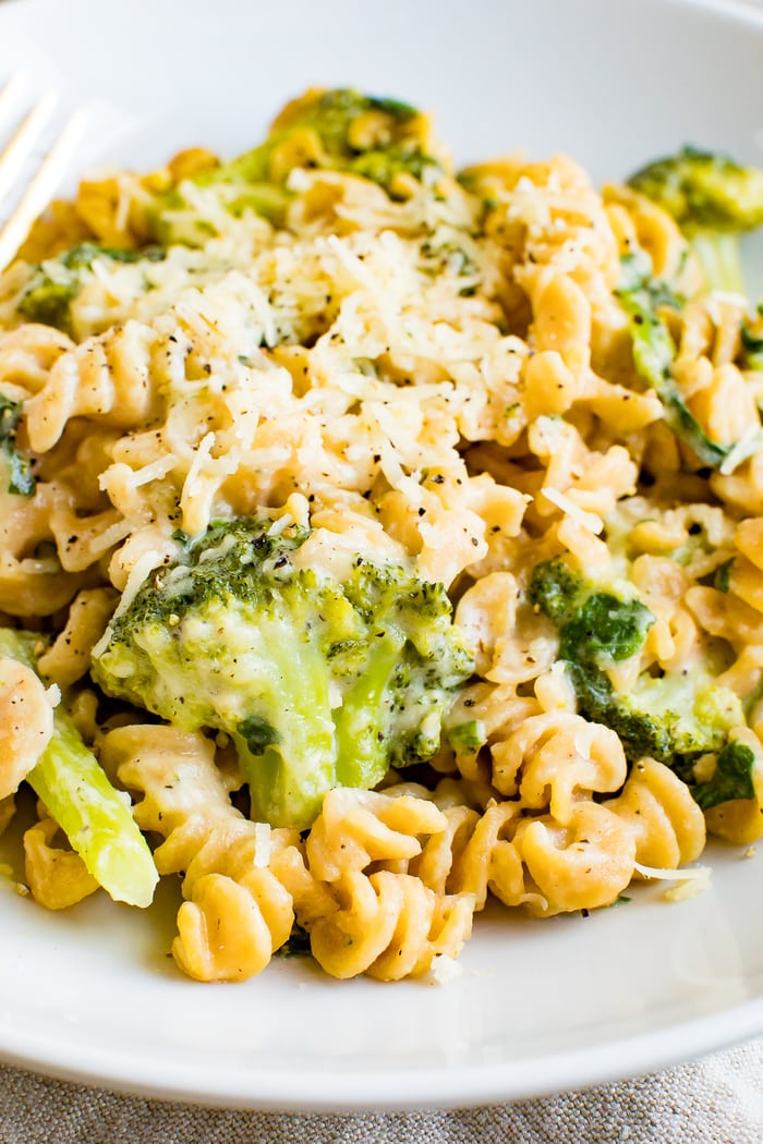 A bowl of creamy, healthy protein packed mac and cheese made with chickpea pasta, broccoli and spinach. Macaroni is topped with extra cheddar.