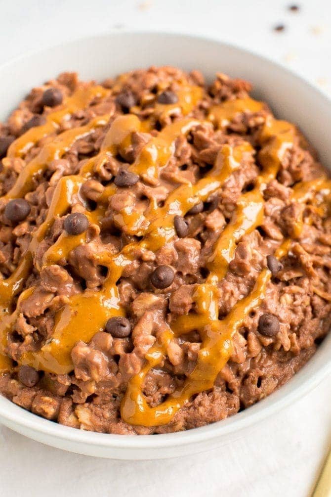 Chocolate peanut butter oatmeal in a bowl topped with a peanut butter drizzle and chocolate chips.