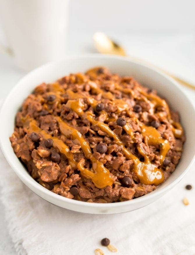 Chocolate peanut butter oatmeal in a bowl topped with a peanut butter drizzle and chocolate chips.