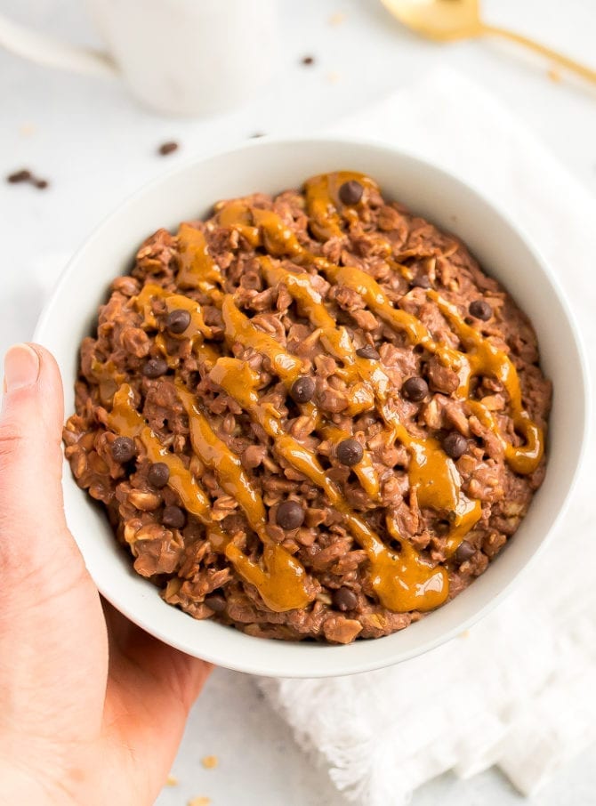 Chocolate peanut butter oatmeal in a bowl topped with a peanut butter drizzle and chocolate chips.