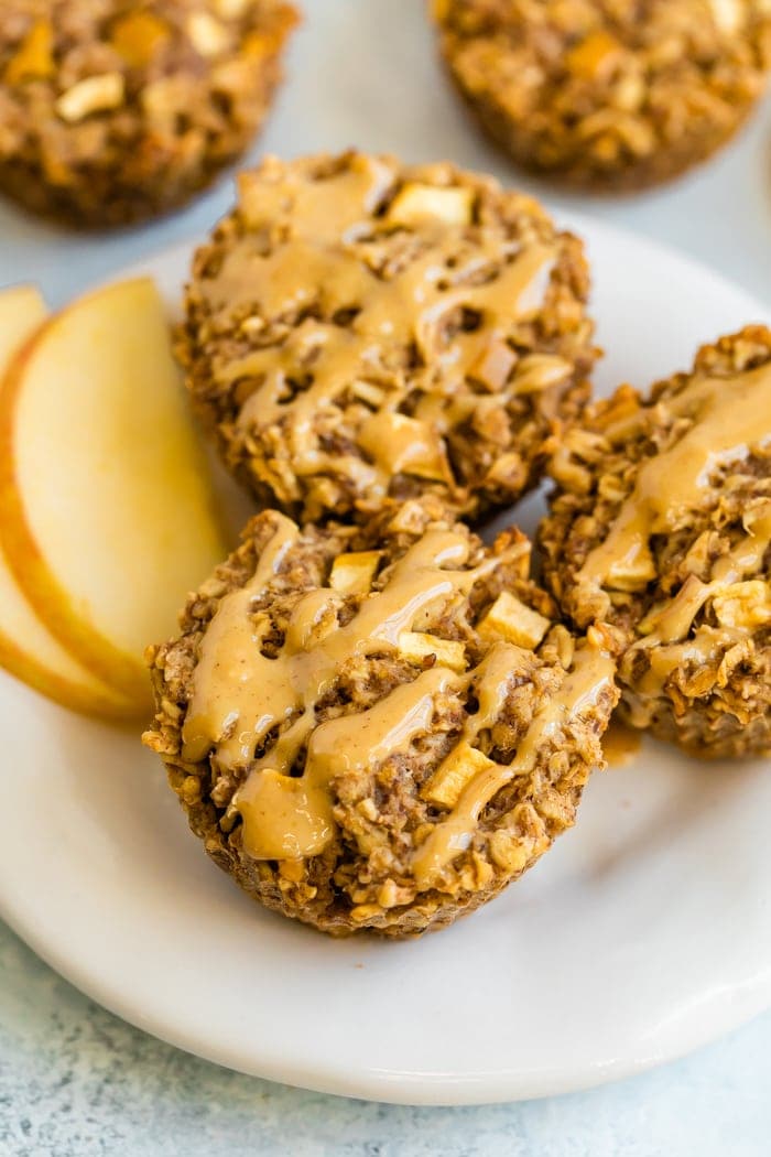 Three apple oatmeal cups on a plate drizzled with peanut butter.