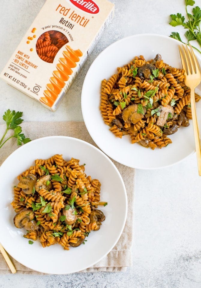 Plates of vegan mushroom stroganoff next to a box of Barilla red lentil rotini.