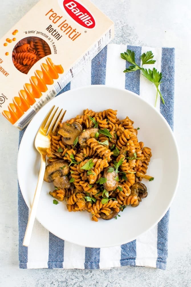 Vegan mushroom stroganoff on a plate next to a box of Barilla red lentil rotini.