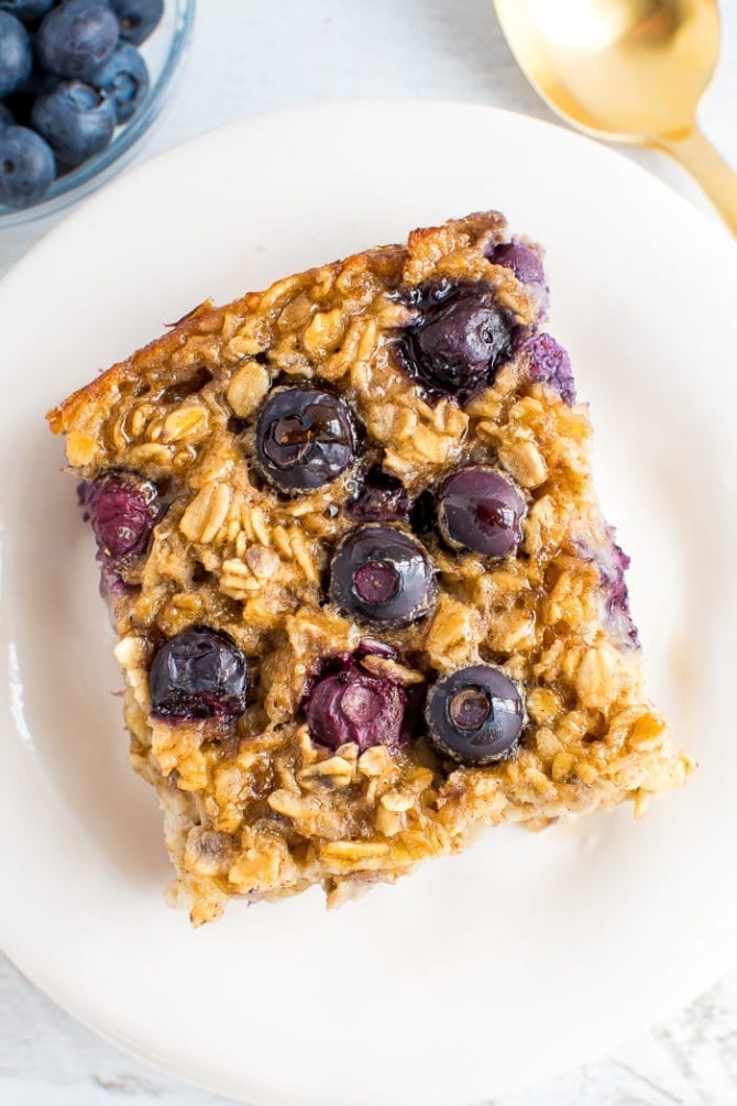 A slice of blueberry baked oatmeal topped with fresh blueberries and maple syrup.