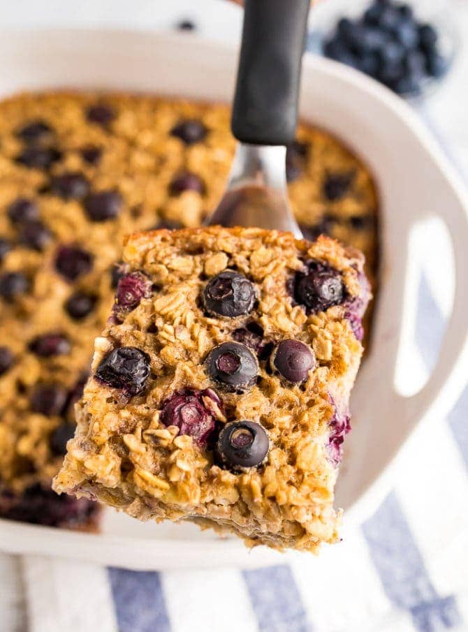 A slice of blueberry baked oatmeal on a spatula being taken out of a baking dish.