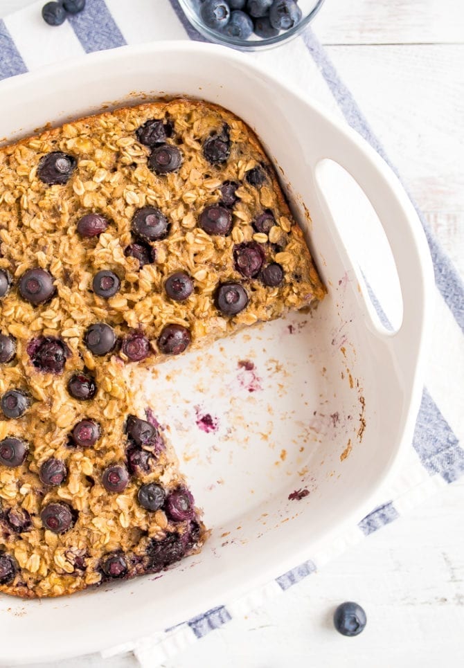 Baking dish with Blueberry Baked Oatmeal topped with fresh blueberries. A slice is taken out of the oatmeal.