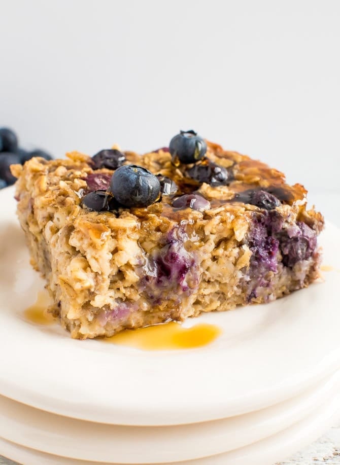 A slice of blueberry baked oatmeal topped with fresh blueberries and maple syrup.