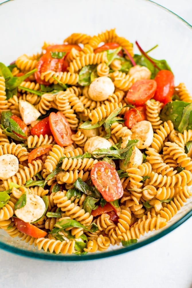 Serving bowl of gluten free caprese pasta salad with tomatoes, mozzarella, basil and a balsamic vinaigrette.