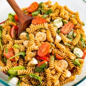 Serving bowl of gluten free caprese pasta salad with tomatoes, mozzarella, basil and a balsamic vinaigrette.