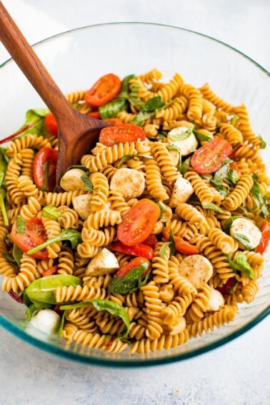 Serving bowl of gluten free caprese pasta salad with tomatoes, mozzarella, basil and a balsamic vinaigrette.