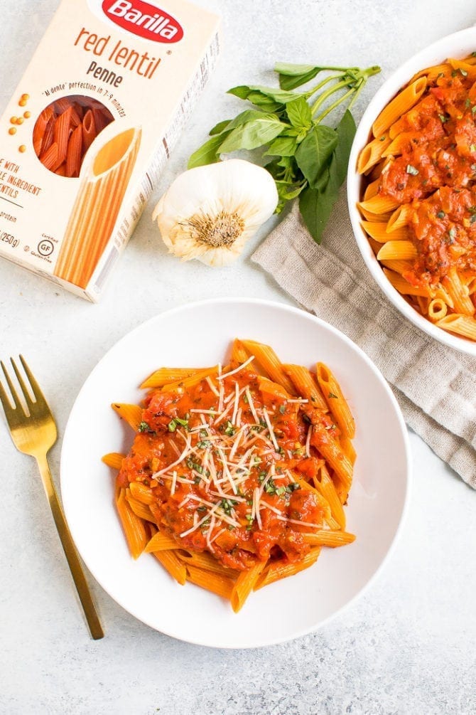 Plate and serving bowl of vegan penne alla vodka next to a box of Barilla red lentil penne.