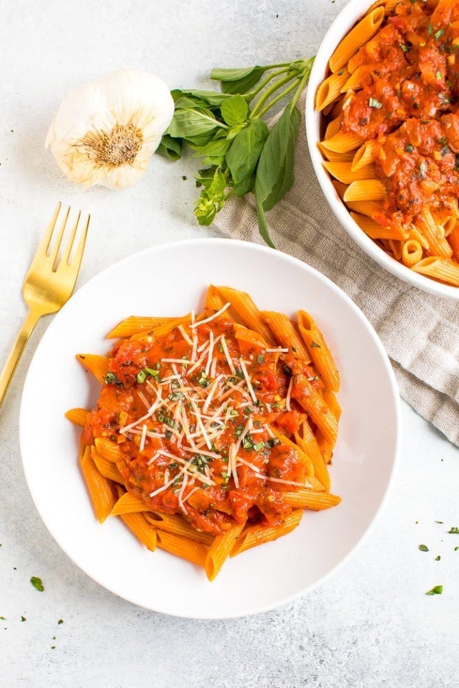 Healthy and vegan penne alla vodka on a plate next to garlic and fresh basil.