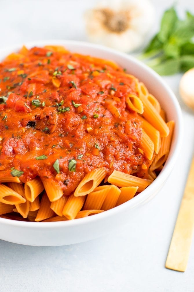 Serving bowl of vegan penne alla vodka topped with fresh basil.