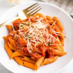 Healthy and vegan penne alla vodka on a plate next to garlic and fresh basil.