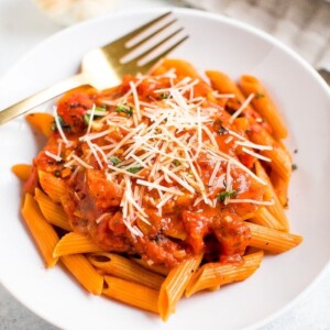 Healthy and vegan penne alla vodka on a plate next to garlic and fresh basil.