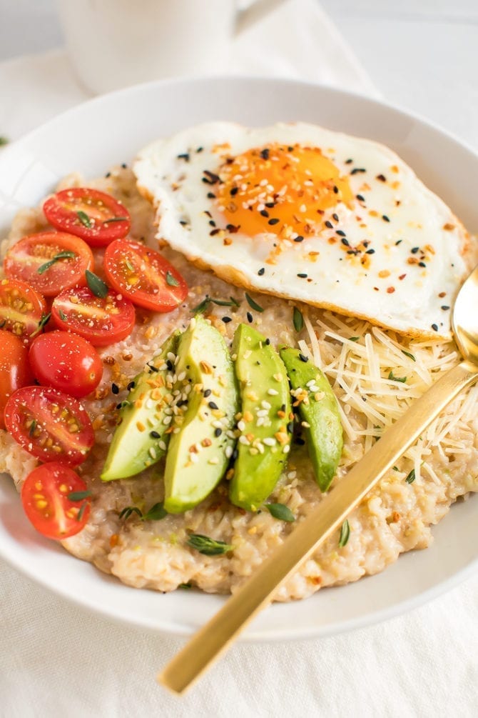 Savory oatmeal topped with avocado, tomatoes, herbs, a fried egg, parmesan, and everything bagel seasoning.