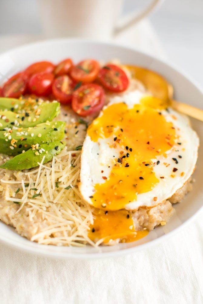 Savory oatmeal topped with avocado, tomatoes, herbs, a fried egg, parmesan, and everything bagel seasoning.