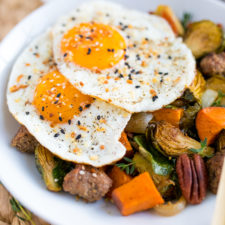 Sweet potato hash with brussel sprouts and pecans, topped with two over easy eggs, on a white plate.