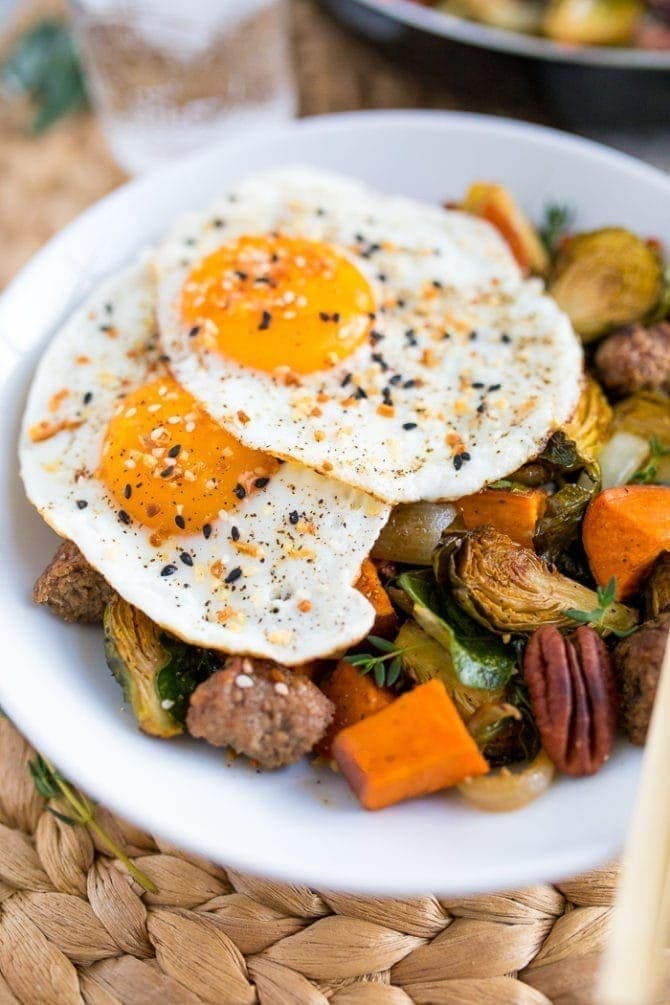 Breakfast hash on a plate with Brussels, pecans, sausage, and roasted sweet potatoes. Topped with two fried eggs and everything bagel spice.