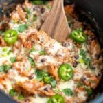 Vegetarian Mexican quinoa casserole in a slow cooker topped with melted cheese, sliced jalapeno, green onions and cilantro.