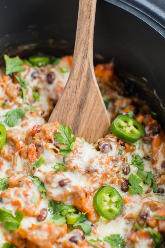 Vegetarian Mexican quinoa casserole in a slow cooker topped with melted cheese, sliced jalapeno, green onions and cilantro.