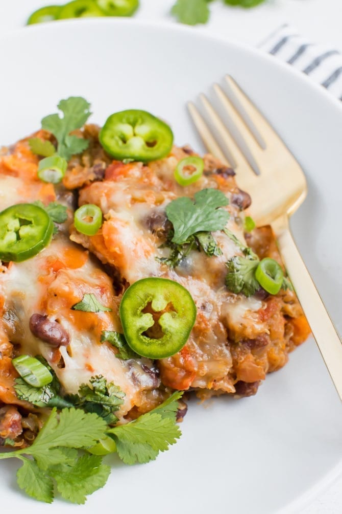 Slow cooker vegetarian Mexican quinoa casserole on a plate topped with melted cheese, jalapeno, cilantro, and green onions.
