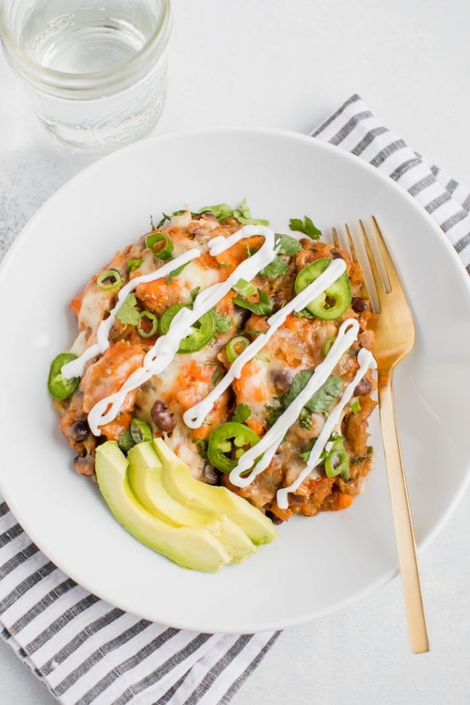 Slow cooker vegetarian Mexican quinoa casserole on a plate topped with melted cheese, sour cream, jalapeno, cilantro, green onions and avocado slices.